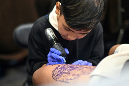 Wielding a cumbersome tattoo gun, nine-year-old Napat Mitmakorn inks the pattern of a fanged serpent on a man's upper thigh Wielding a cumbersome tattoo gun, nine-year-old Napat Mitmakorn inks the pattern of a fanged serpent on a man's upper thigh