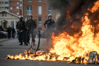 Riot police stand behind burning trash as protesters and high-school students gather outside a high school in Toulouse, France - Ed JONES (AFP)
